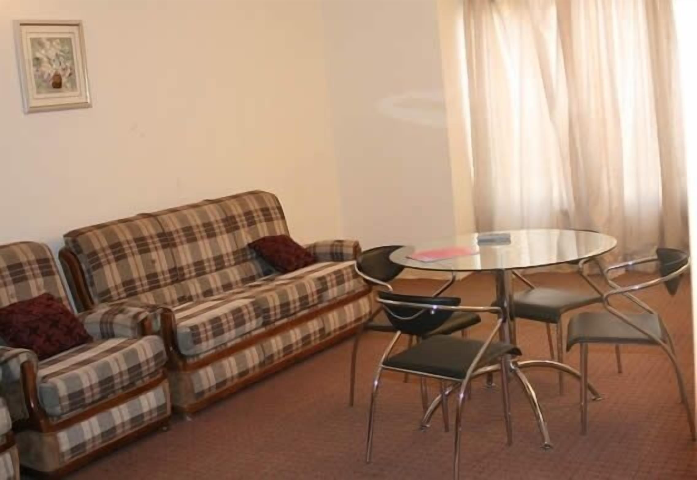 A living room with a plaid sofa, a round glass table, and metal chairs.