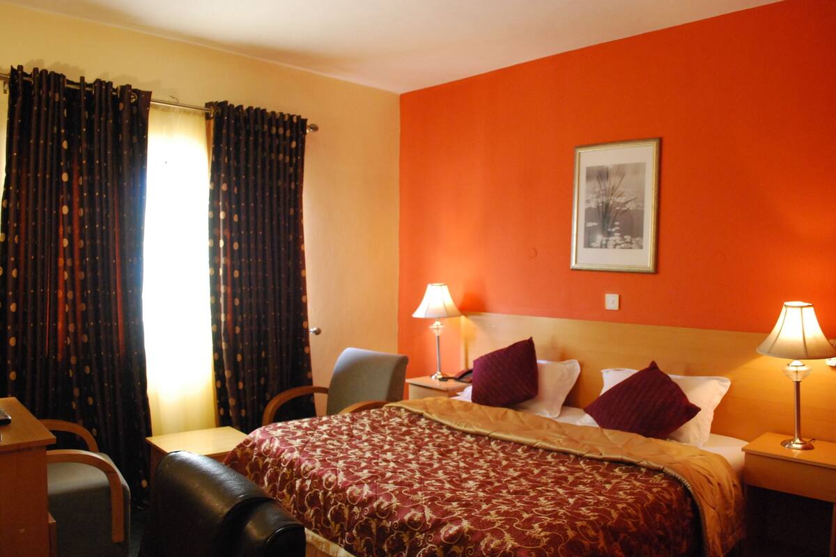 A hotel room with a bed, two bedside lamps, a chair, a desk, and curtains.
