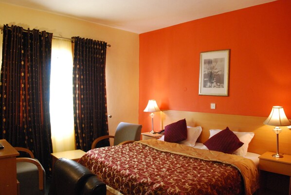 Une chambre d’hôtel avec un lit, deux lampes de chevet, une chaise, un bureau et des rideaux.