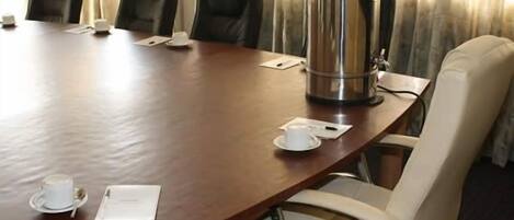A conference room with a large wooden table, four black leather chairs, a coffee pot, and a white cup on the table.