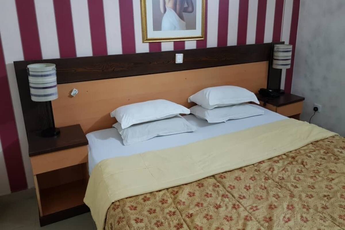 A hotel room with a striped wall, a bed with white linens, a wooden headboard, two bedside tables with lamps, and a framed picture on the wall.