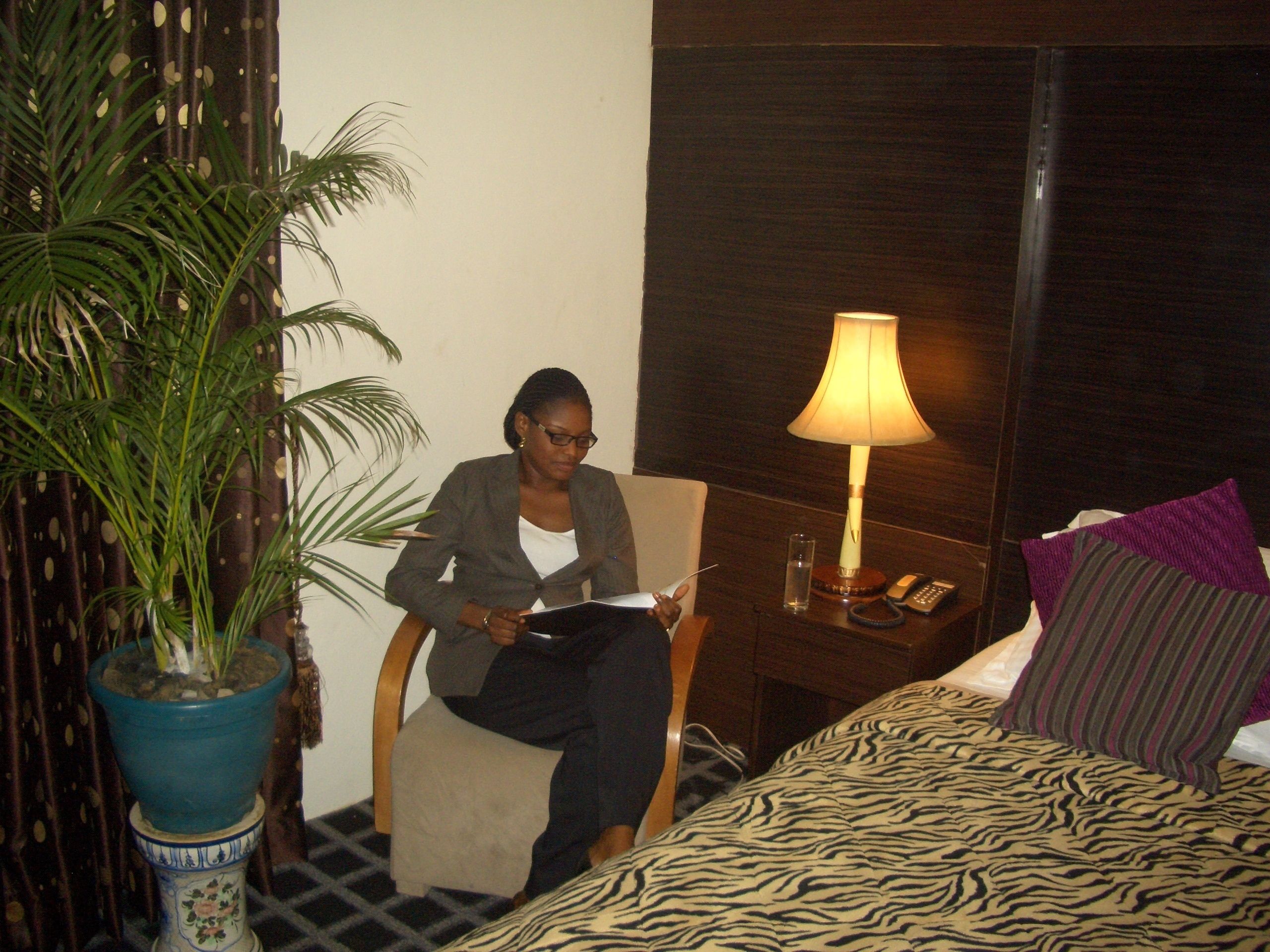 Een hotelkamer met een bed, een stoel, een lamp en een potplant.