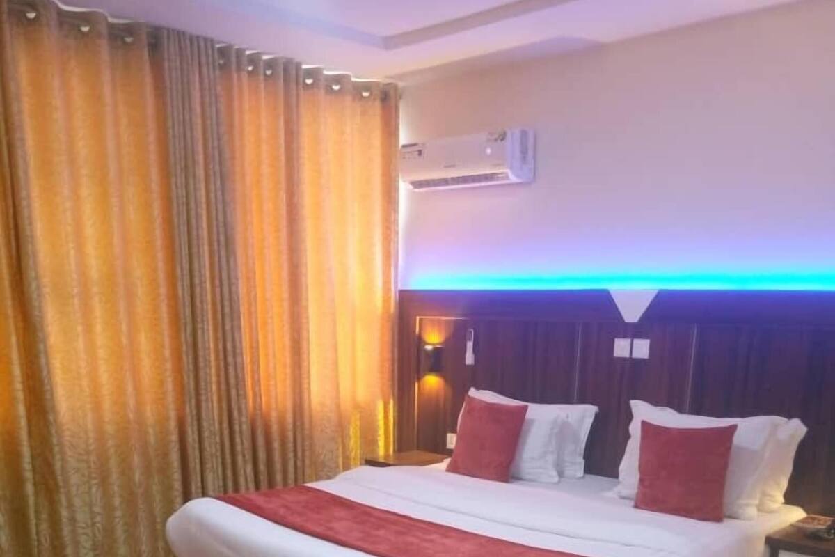 A hotel room with a bed, curtains, an air conditioning unit, and a nightstand.