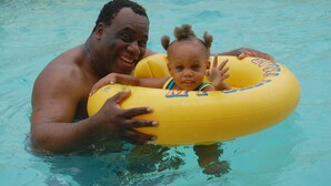 Un homme et un enfant dans une piscine, tous les deux portant des bouées gonflables jaunes.