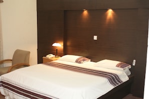 A hotel room with a large bed, a bedside lamp, a chair, and a telephone on the nightstand. - Citilodge Hotel Lagos (Lekki)