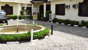 Une cour avec une fontaine, un chemin pavé et un bâtiment équipé de climatiseurs.