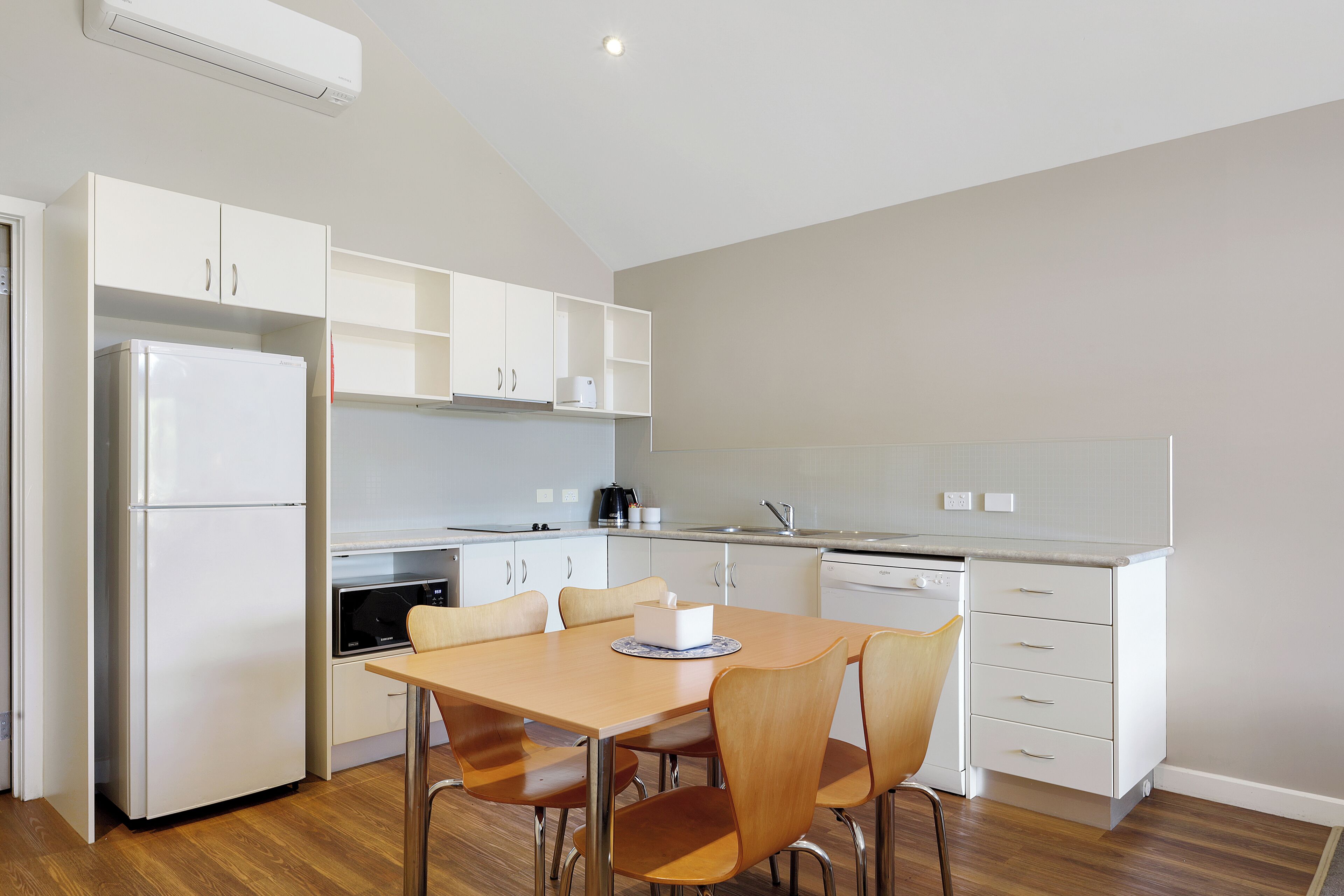 Una cocina moderna con armarios blancos, un refrigerador, una estufa y una mesa de comedor con sillas.