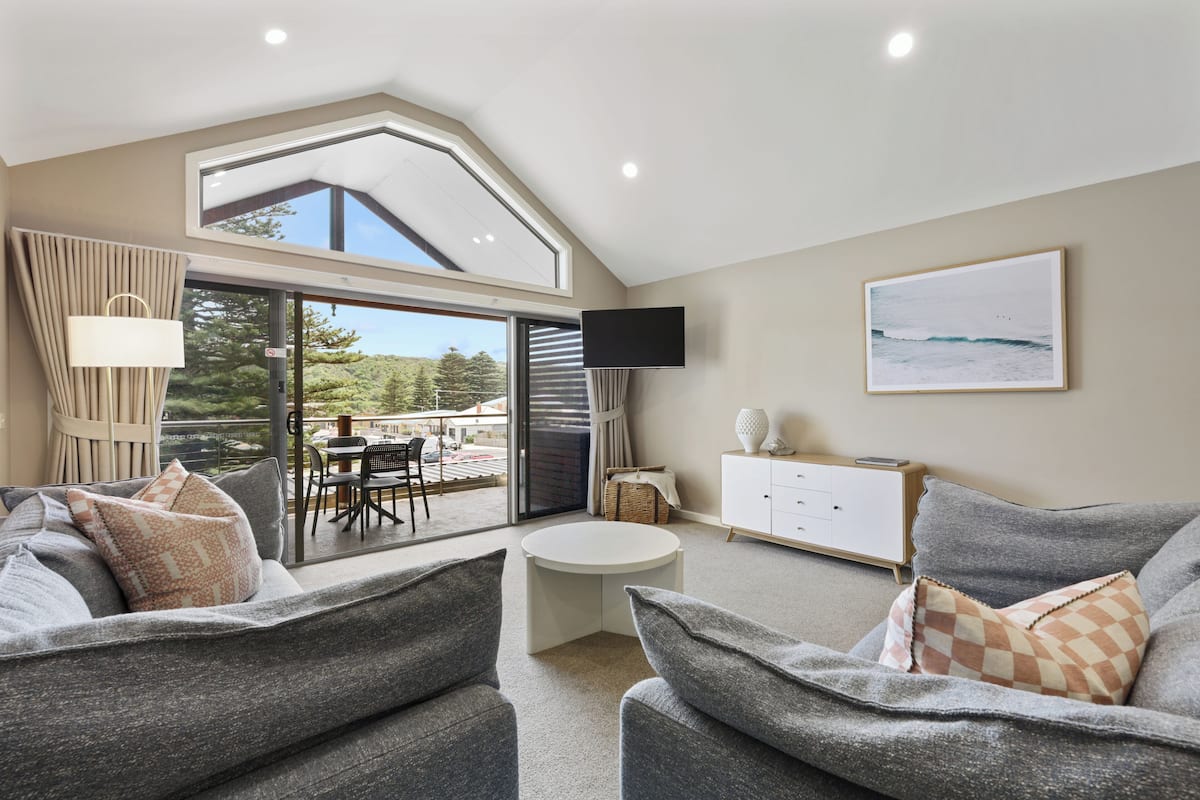 A modern living room with a sofa, a small round table, and a TV mounted on the wall.
