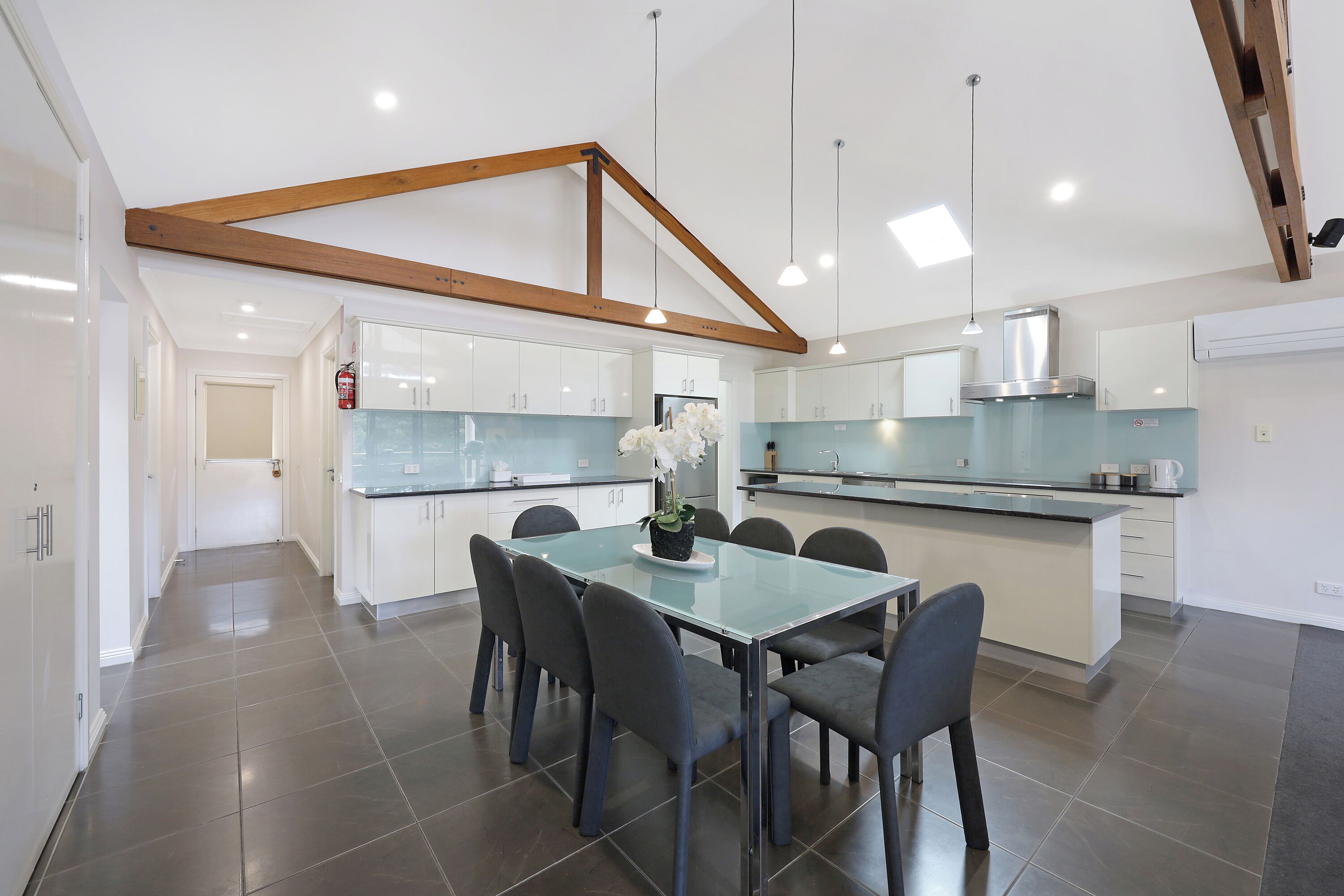 Una cocina moderna con armarios blancos, una isla central y una zona de comedor con mesa y sillas de vidrio.