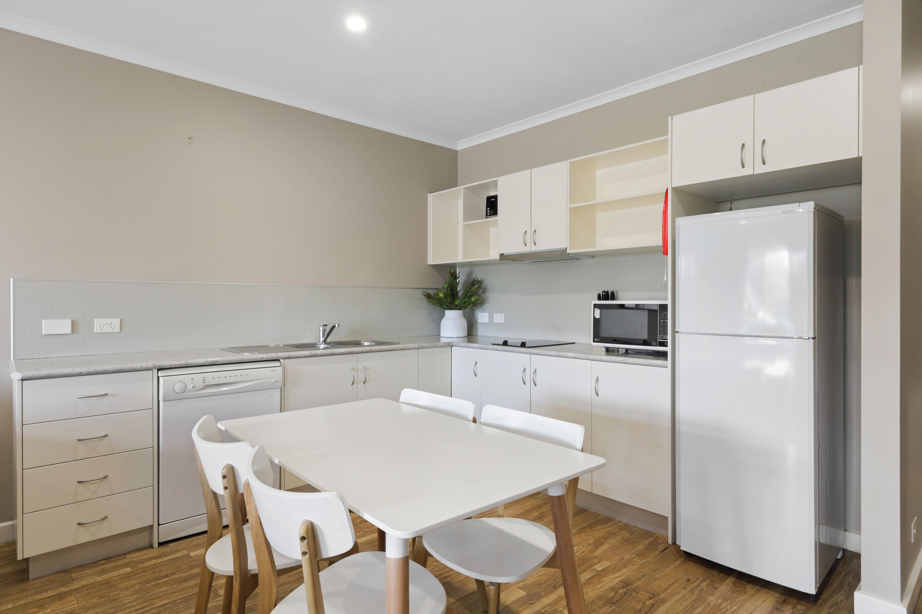 A modern kitchen with white cabinetry, a white dining table with chairs, a built-in oven, and a microwave.