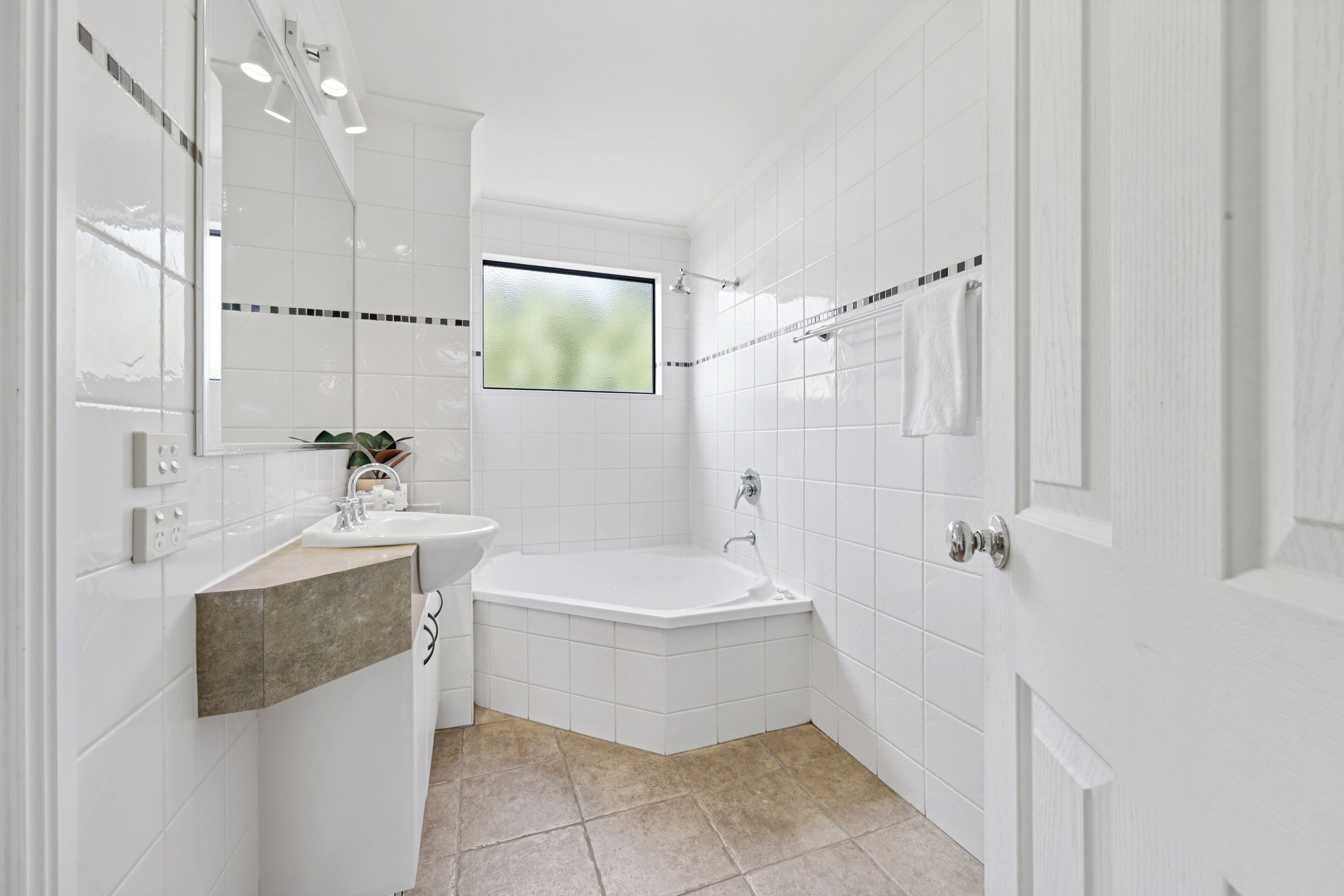 Une salle de bain moderne avec des carreaux blancs, une baignoire, un lavabo et une fenêtre.