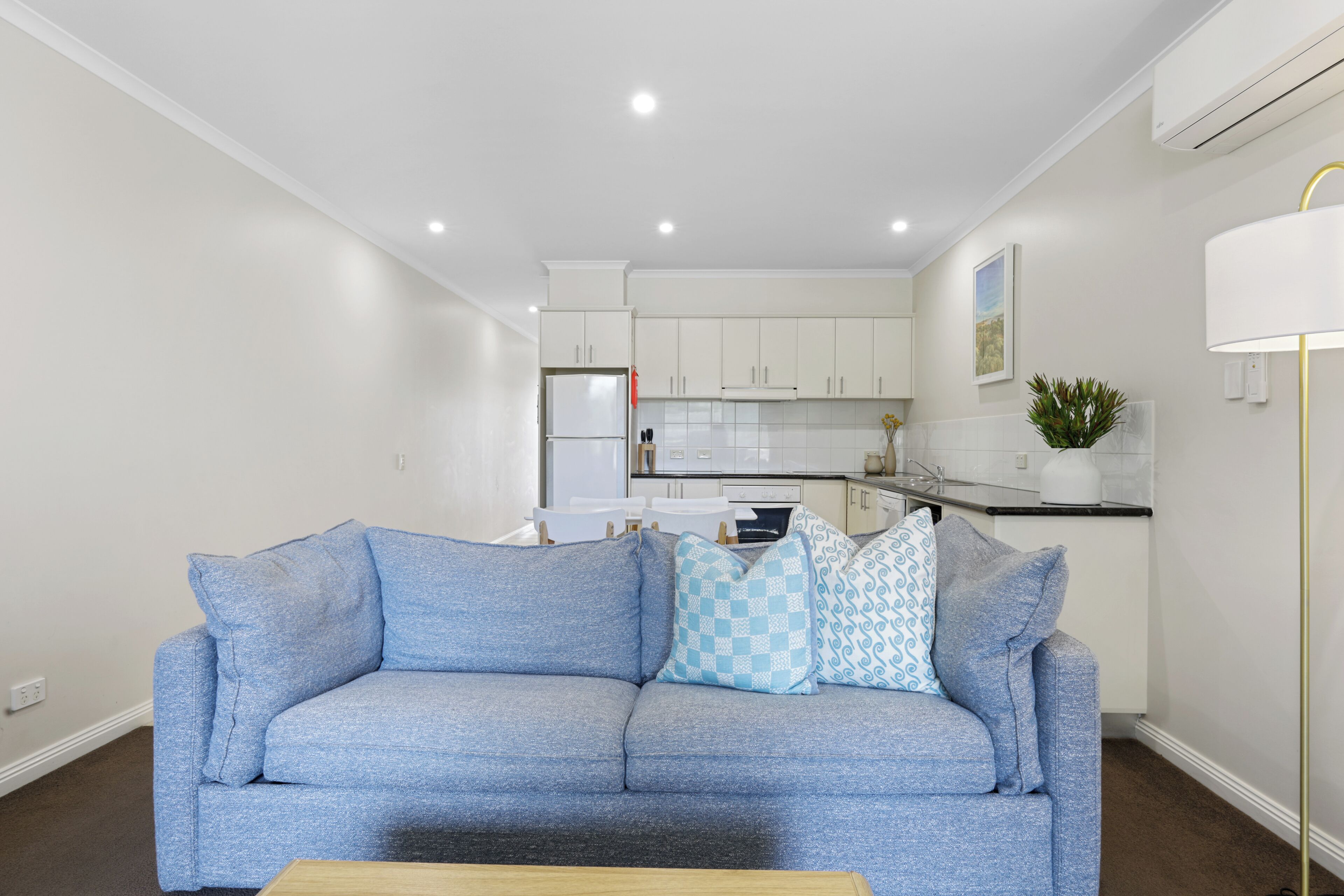 Una sala de estar moderna con un sofá azul, una mesa de centro y una cocina al fondo.