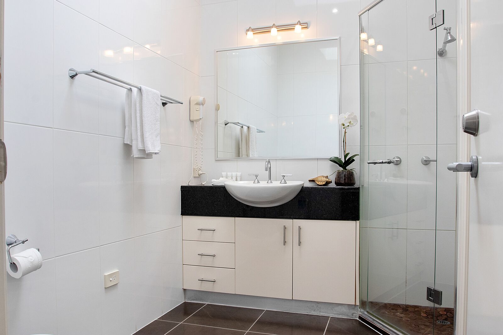 Un baño moderno con lavamanos blanco, encimera negra y cabina de ducha de vidrio.
