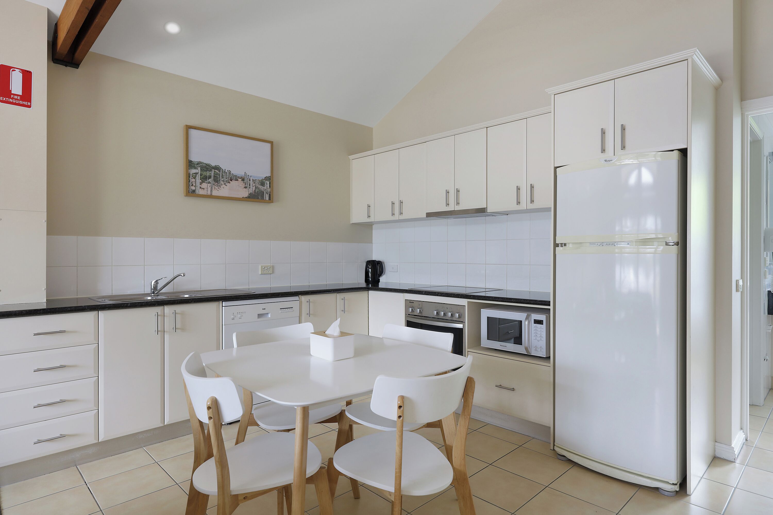 Une cuisine moderne avec des meubles blancs, une table à manger et quatre chaises, un réfrigérateur, un four et un four à micro-ondes.