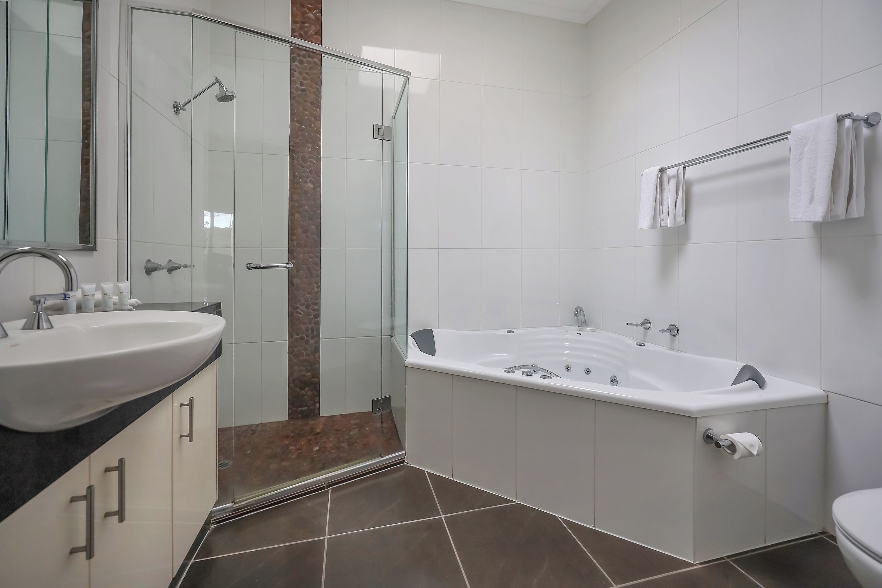 Een moderne badkamer met een douchecabine van glas, een ruime badkuip, een witte wastafel en een toilet.