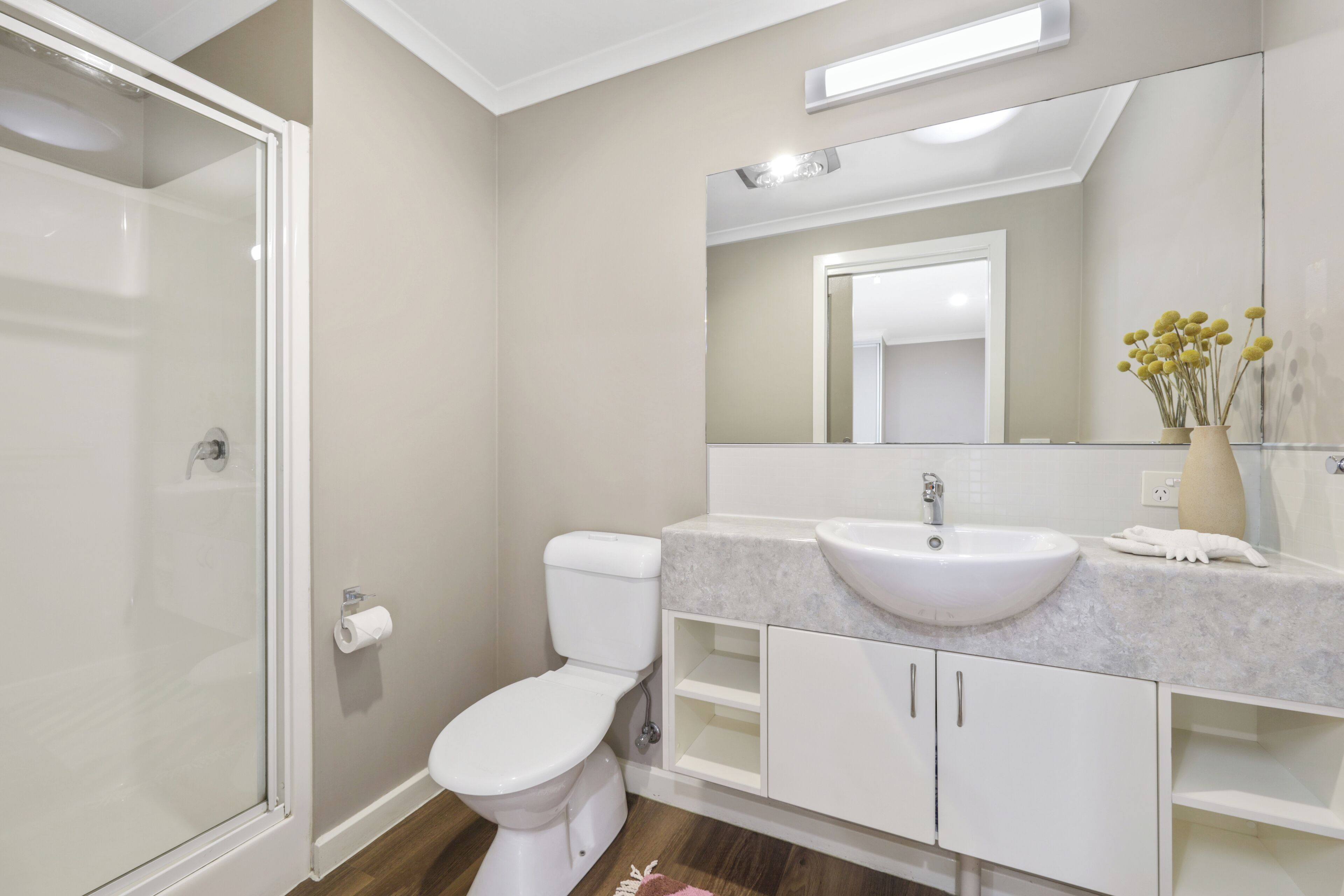 Et moderne badeværelse med en glasbrusekabine, et hvidt toilet, en marmorvask og et stort spejl.