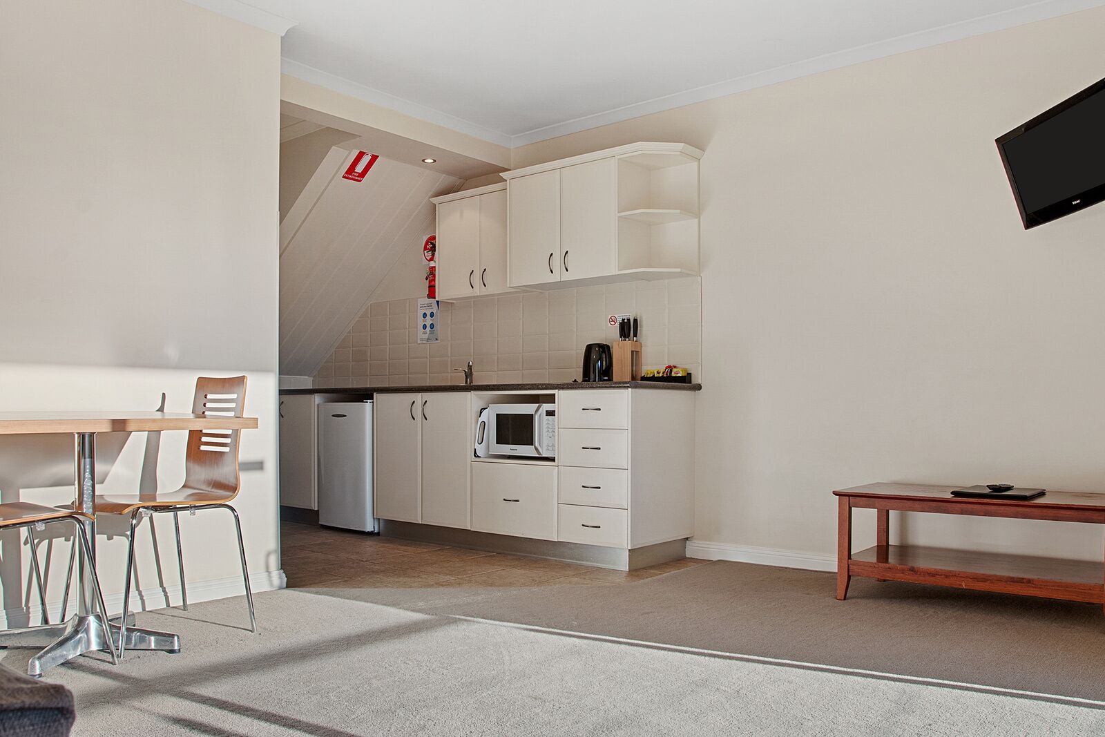 A modern kitchen with white cabinets, a microwave, and a coffee maker. There is a dining area with a table and chairs.