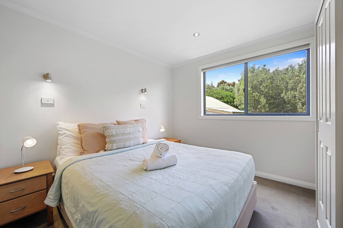 A bedroom with a large bed, bedside lamps, a nightstand, and a window with a view of trees.