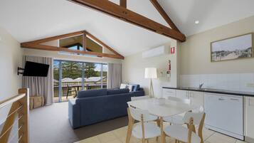 A modern living room with a blue sofa, a white dining table with chairs, and a kitchen area with white cabinets and a dishwasher.