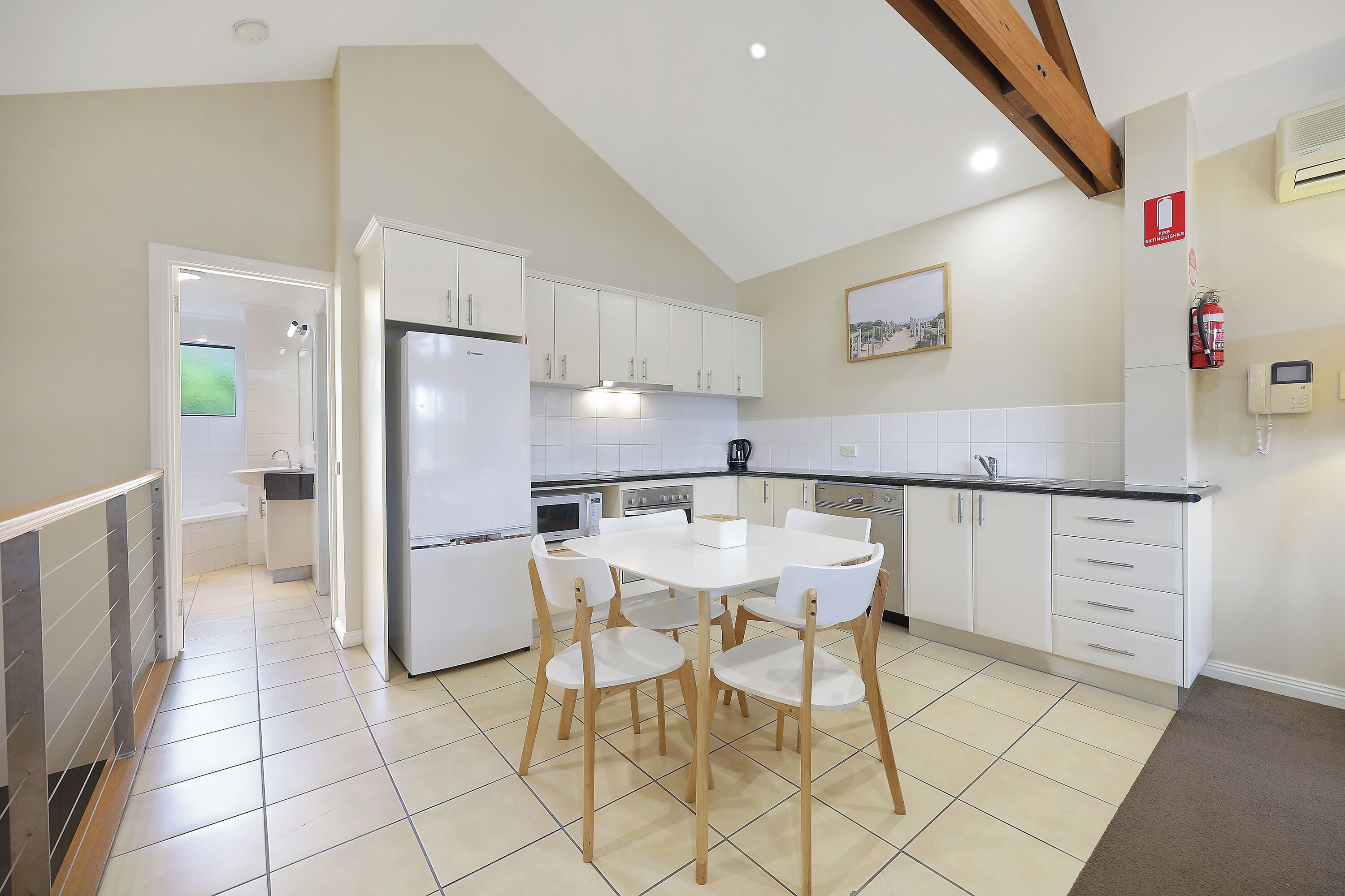 Una cocina moderna con armarios blancos, una isla central y una zona de comedor con cuatro sillas.