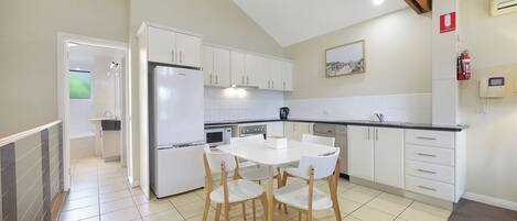 Una cocina moderna con armarios blancos, una isla central y una zona de comedor con cuatro sillas.