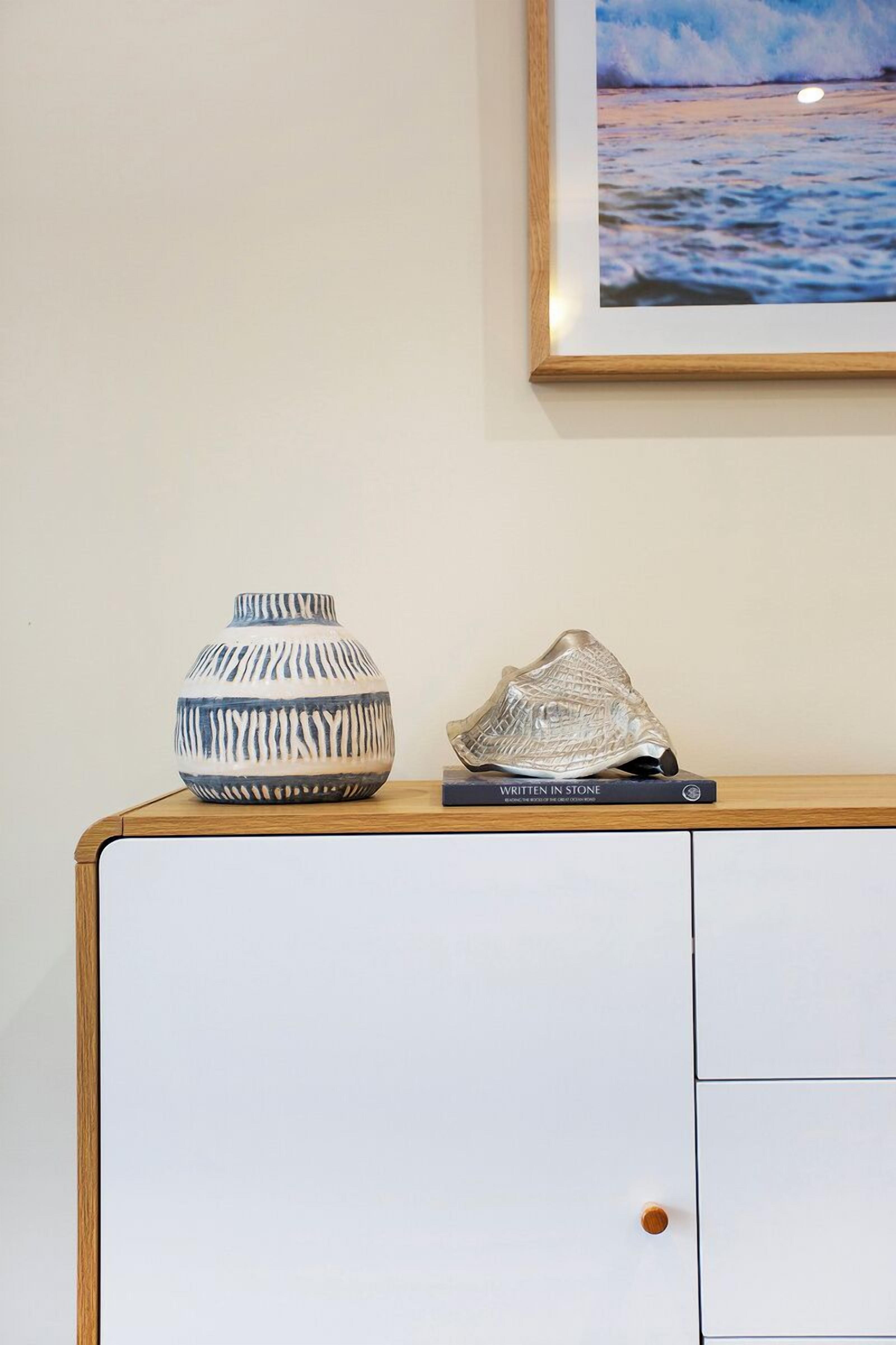 A white cabinet with a wooden top, a blue and white vase, and a silver sculpture on top.