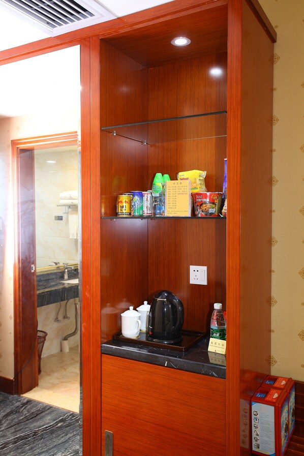 A wooden cabinet with shelves containing various items, a countertop with a kettle, and a box of tissues.