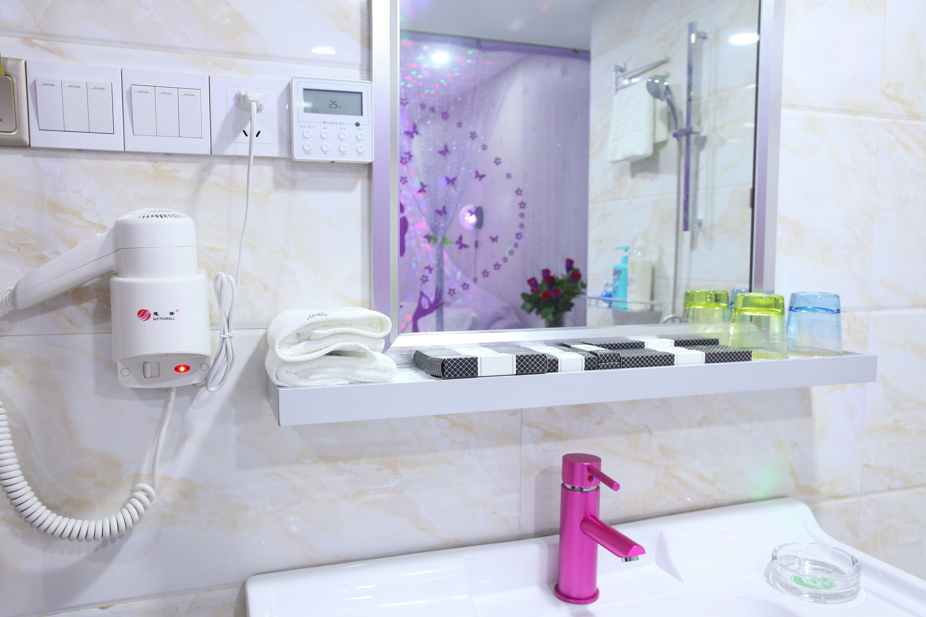 Un baño con un lavabo blanco, un grifo rosa, un secador de pelo, un perchero para toallas y un estante con artículos de aseo.