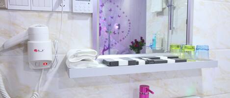 Un baño con un lavabo blanco, un grifo rosa, un secador de pelo, un perchero para toallas y un estante con artículos de aseo.