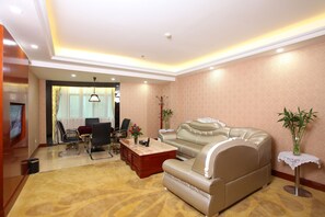 A living room with a beige sofa, a coffee table, a TV, and a dining area with chairs and a table. - BORRMAN Hotel (Guangzhou)