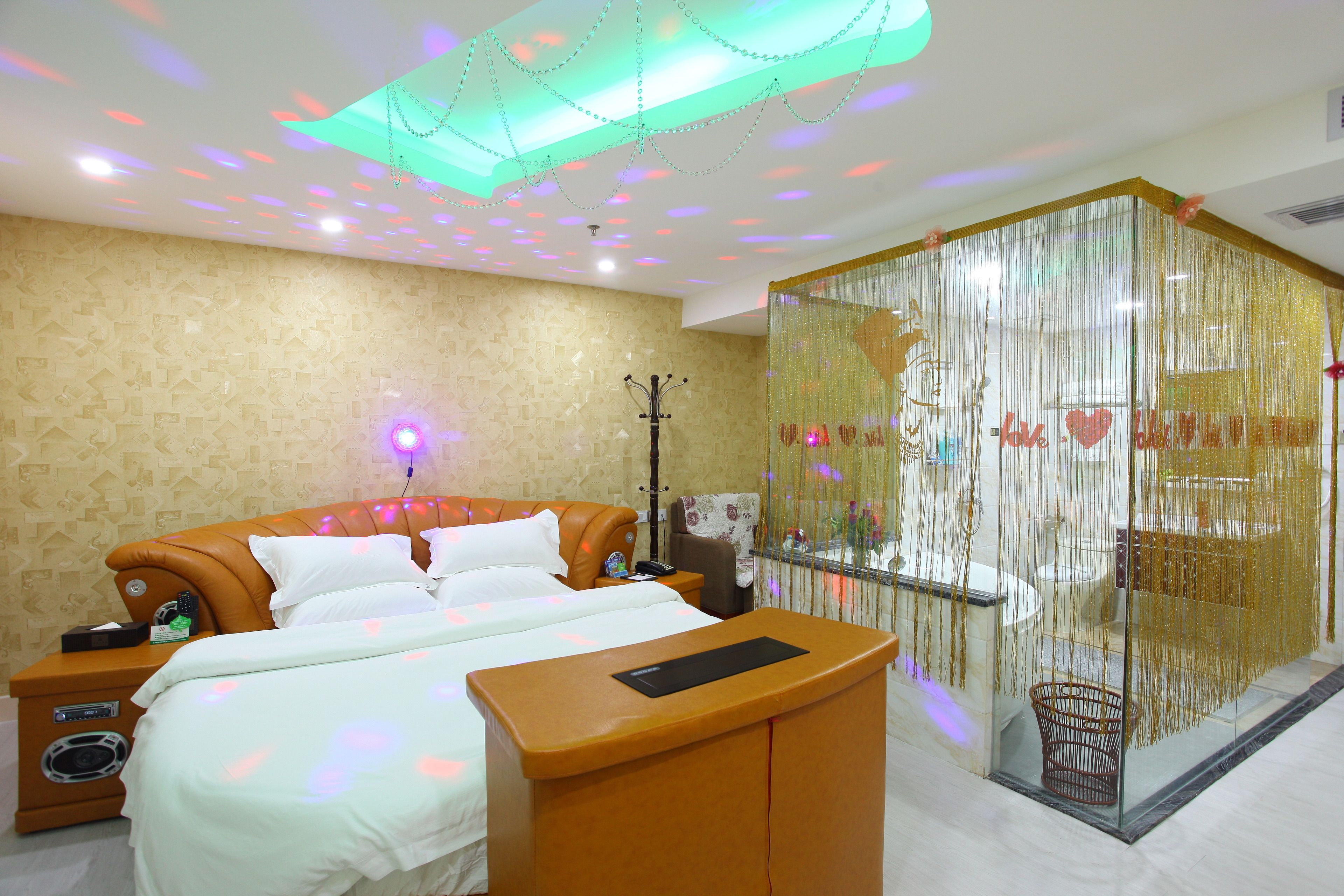 A hotel room with a bed, bedside tables, a desk, and a glass partition with decorative elements.