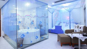 A room with a glass partition, a round bathtub, a blue chair, and a small table with a lace tablecloth. - BORRMAN Hotel (Guangzhou)
