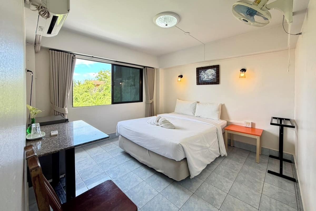 Una habitación de hotel con cama, escritorio, silla y ventana con cortinas.