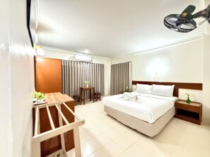 Una habitación de hotel con cama, mesita de noche, lámpara y un pequeño escritorio con silla.