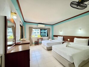 A hotel room with two beds, a desk, a chair, a mirror, a window with curtains, and an air conditioning unit. - J Mansion (Krabi)