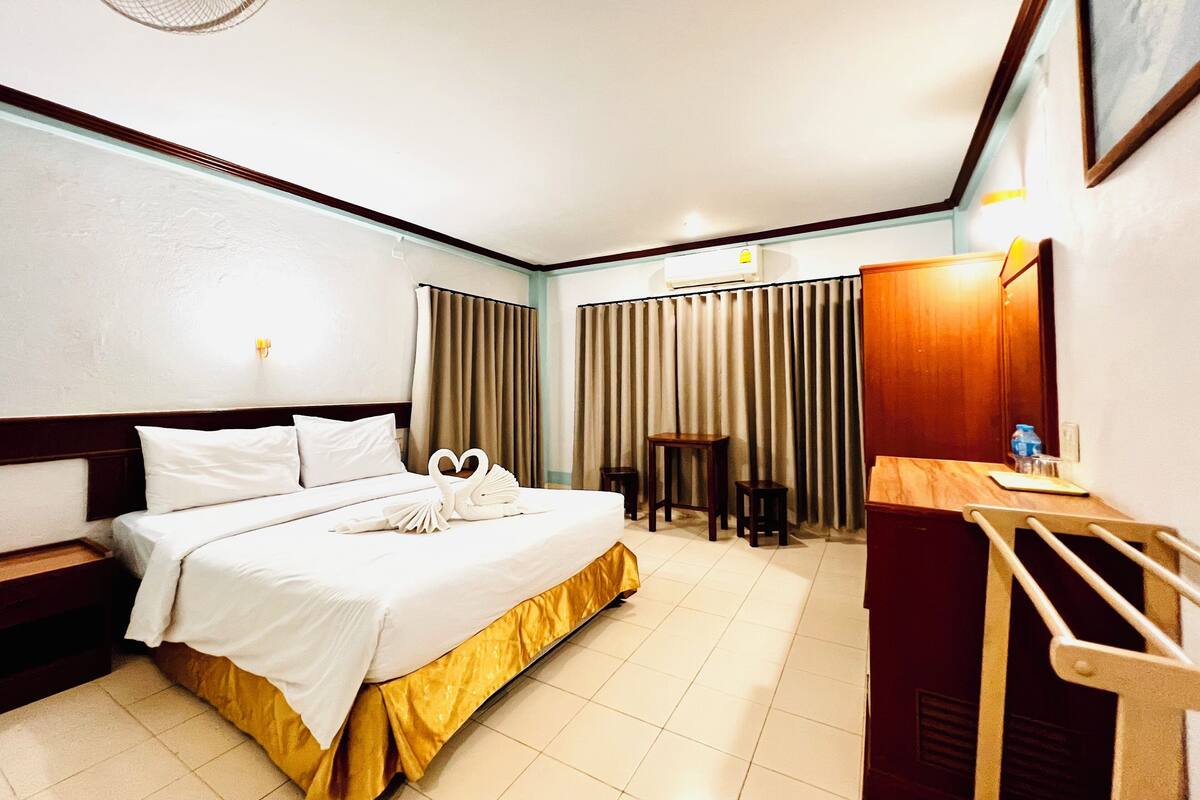 Habitación de hotel con cama, mesitas de noche, escritorio, silla, unidad de aire acondicionado y espejo.