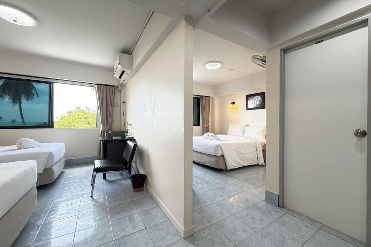Habitación de hotel con dos camas, un escritorio, una silla, una mesita y un ventanal con cortinas.