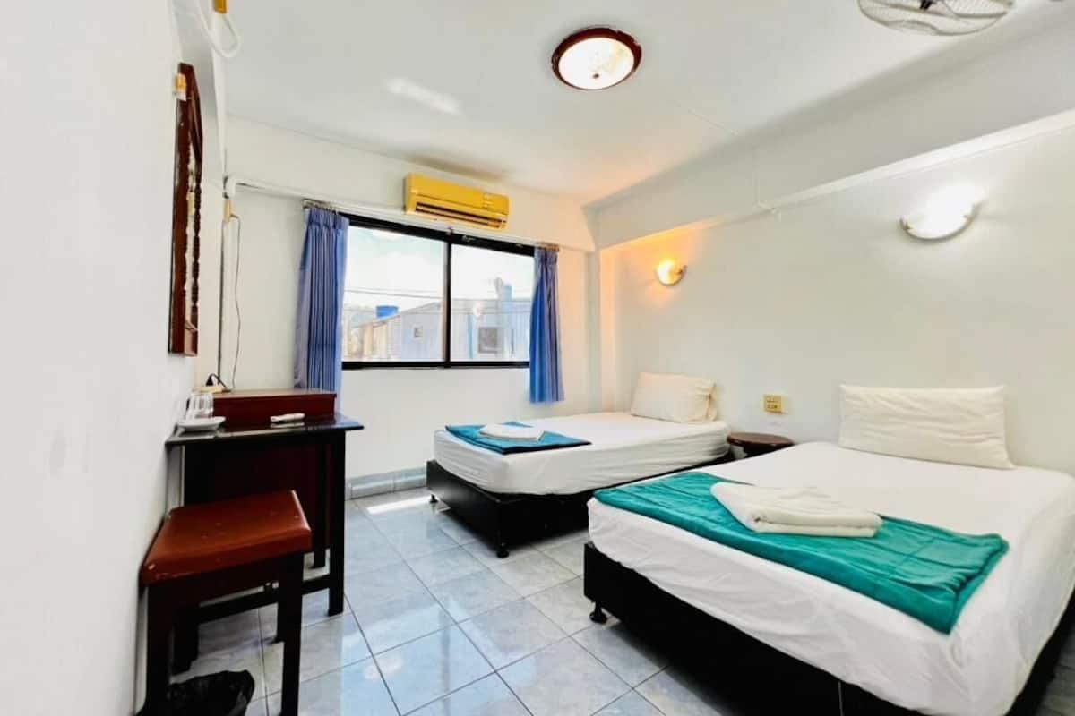 Habitación de hotel con dos camas, un escritorio, una silla, una ventana con cortinas y una lámpara en el techo.