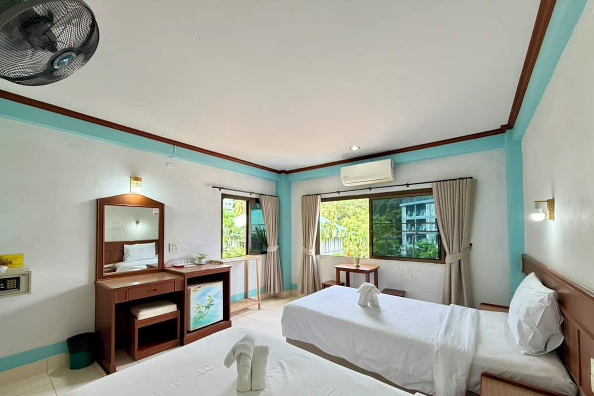 Habitación de hotel con dos camas, un escritorio, una silla, una mesita, un ventilador y una ventana con cortinas.