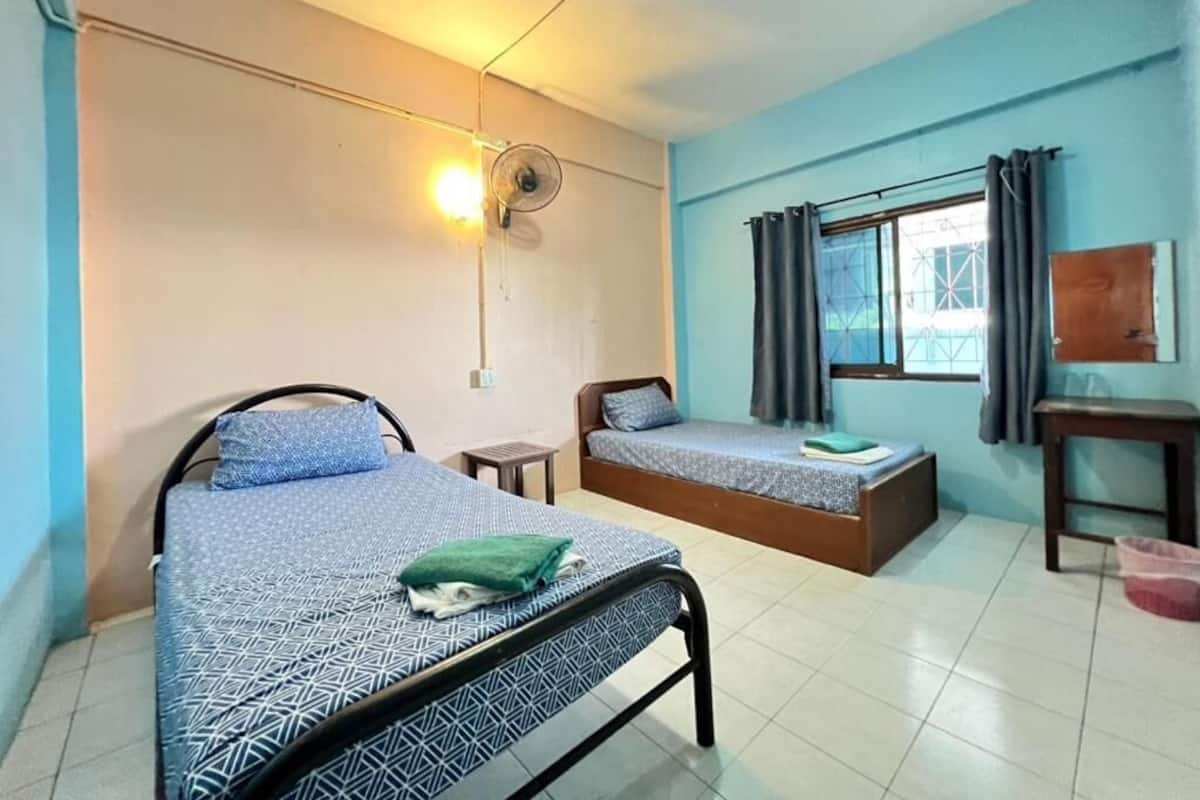 Una habitación con dos camas, un escritorio, una silla, un ventilador y una ventana con cortinas.