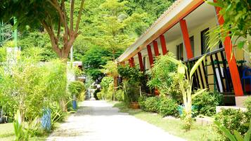Un sendero conduce a un edificio con fachada roja y blanca, rodeado de exuberante vegetación y plantas tropicales.