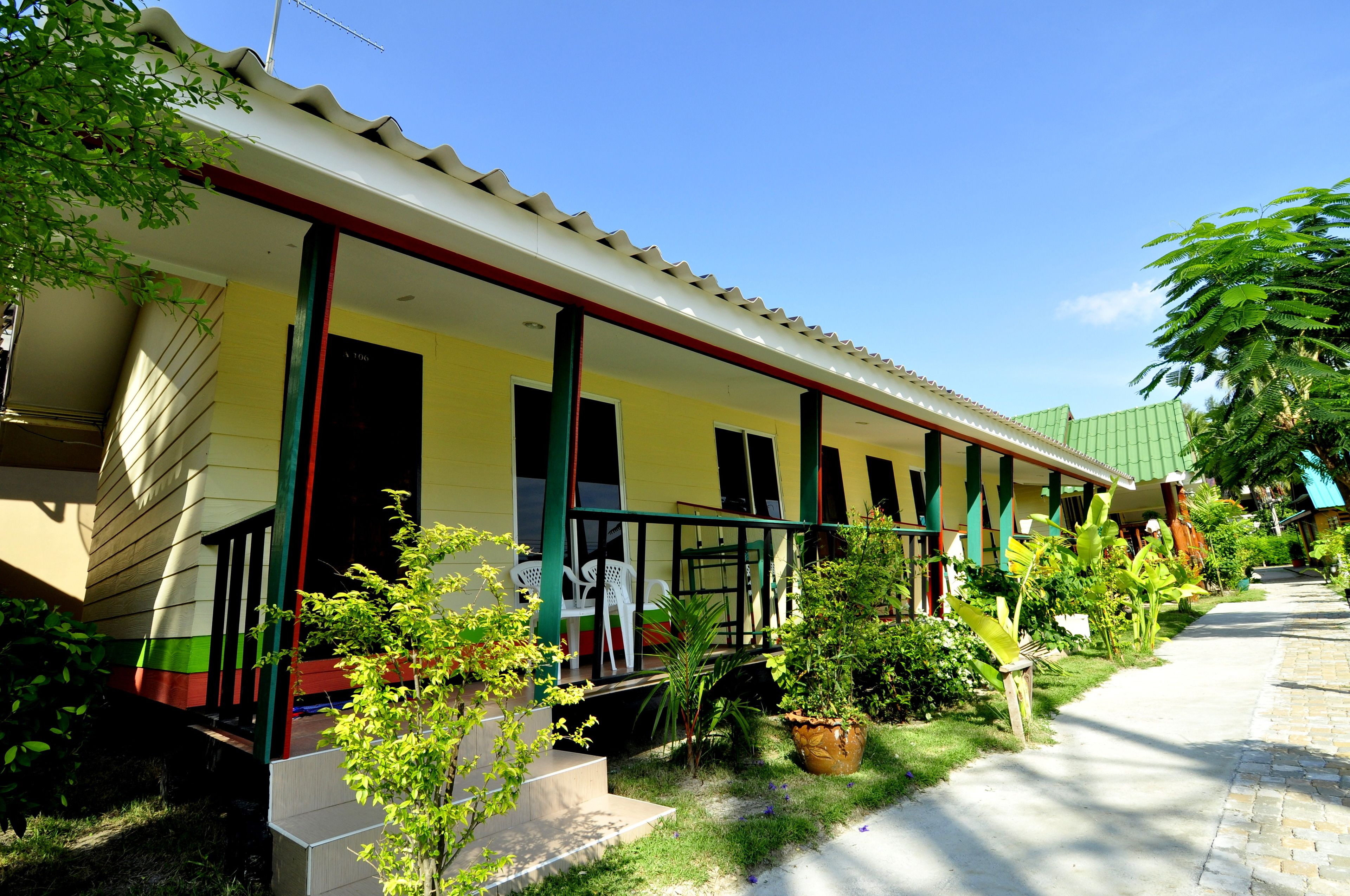 A hotel with a covered porch, outdoor seating, and lush greenery.