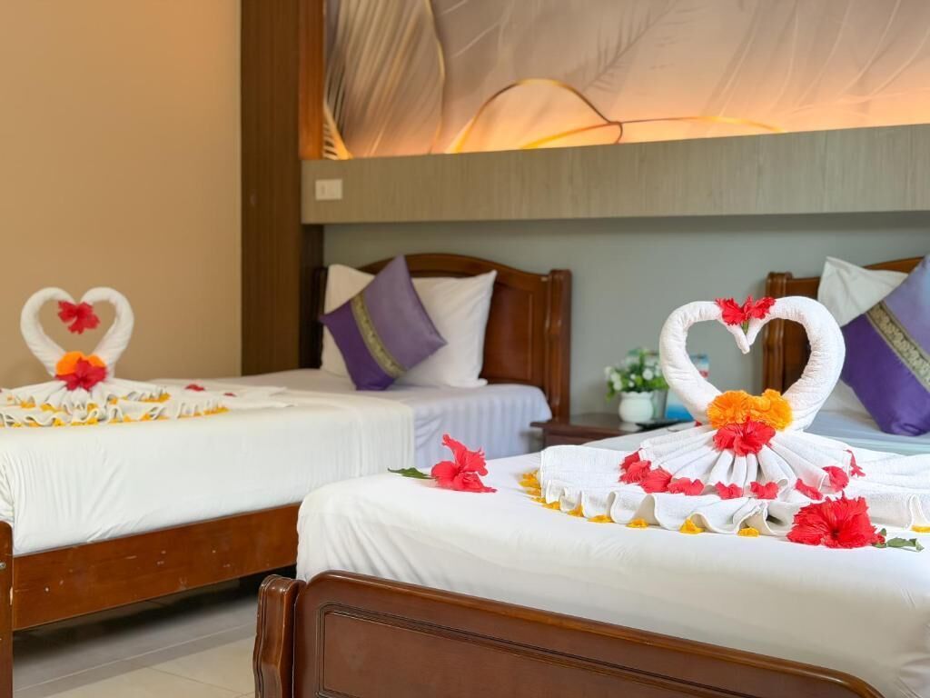 Two twin beds with white linens, each adorned with a heart-shaped towel arrangement and red flowers.