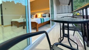 A modern hotel room with a large sliding glass door leading to a balcony, a bed with a wooden headboard, and a small table with chairs. - Chongkhao Resort (Ko Phi Phi)