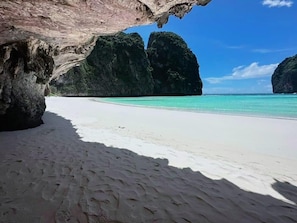 A beach with white sand and clear turquoise water, surrounded by large rock formations.