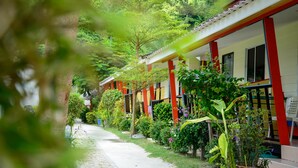 A row of single-story buildings with red and white exteriors, surrounded by lush greenery and a paved pathway. - Chongkhao Resort (Ko Phi Phi)