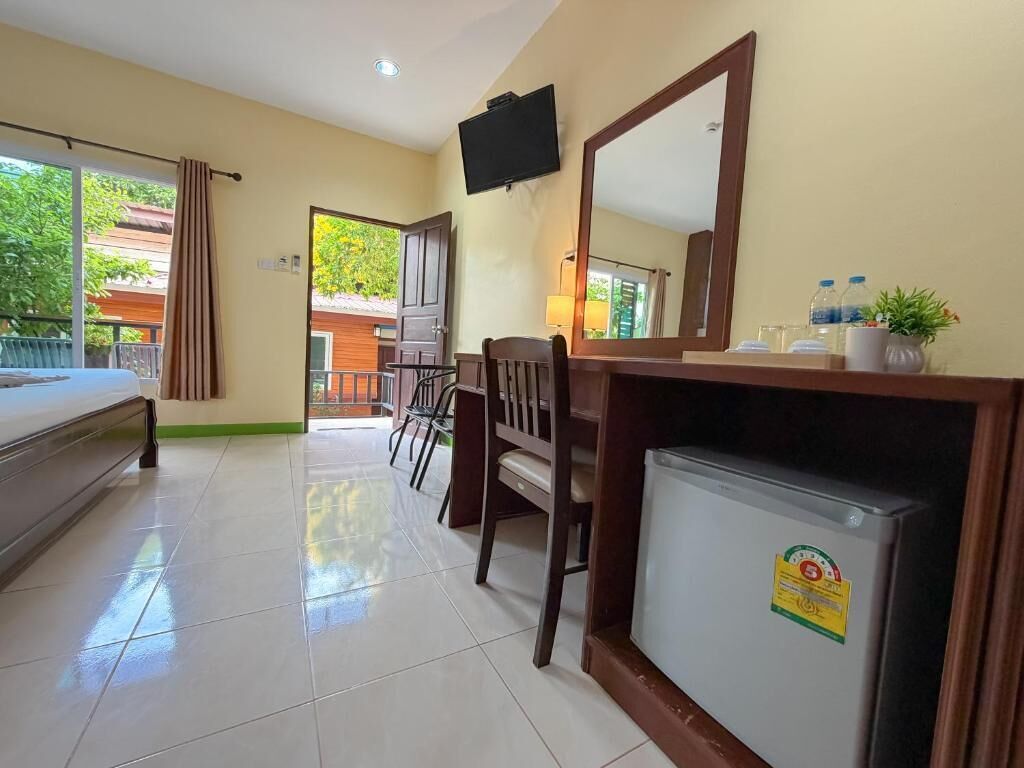 A hotel room with a bed, a desk with a computer, a refrigerator, a TV, and a view of the outside.