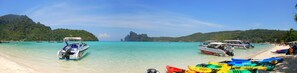 A beach with boats and kayaks, clear turquoise water, and a mountainous backdrop. - Chongkhao Resort (Ko Phi Phi)