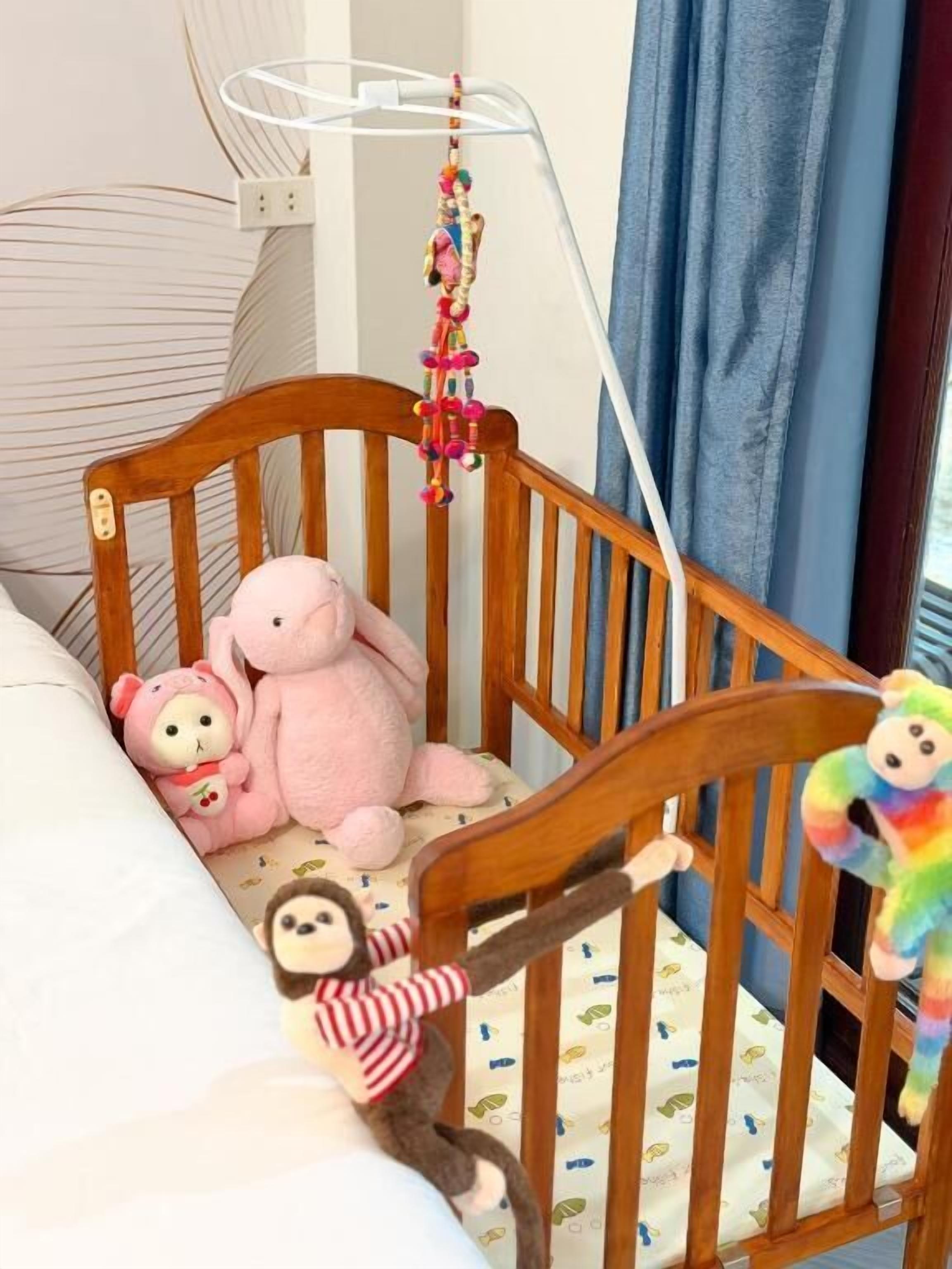 A wooden crib with a white mattress, a hanging mobile, and plush toys.