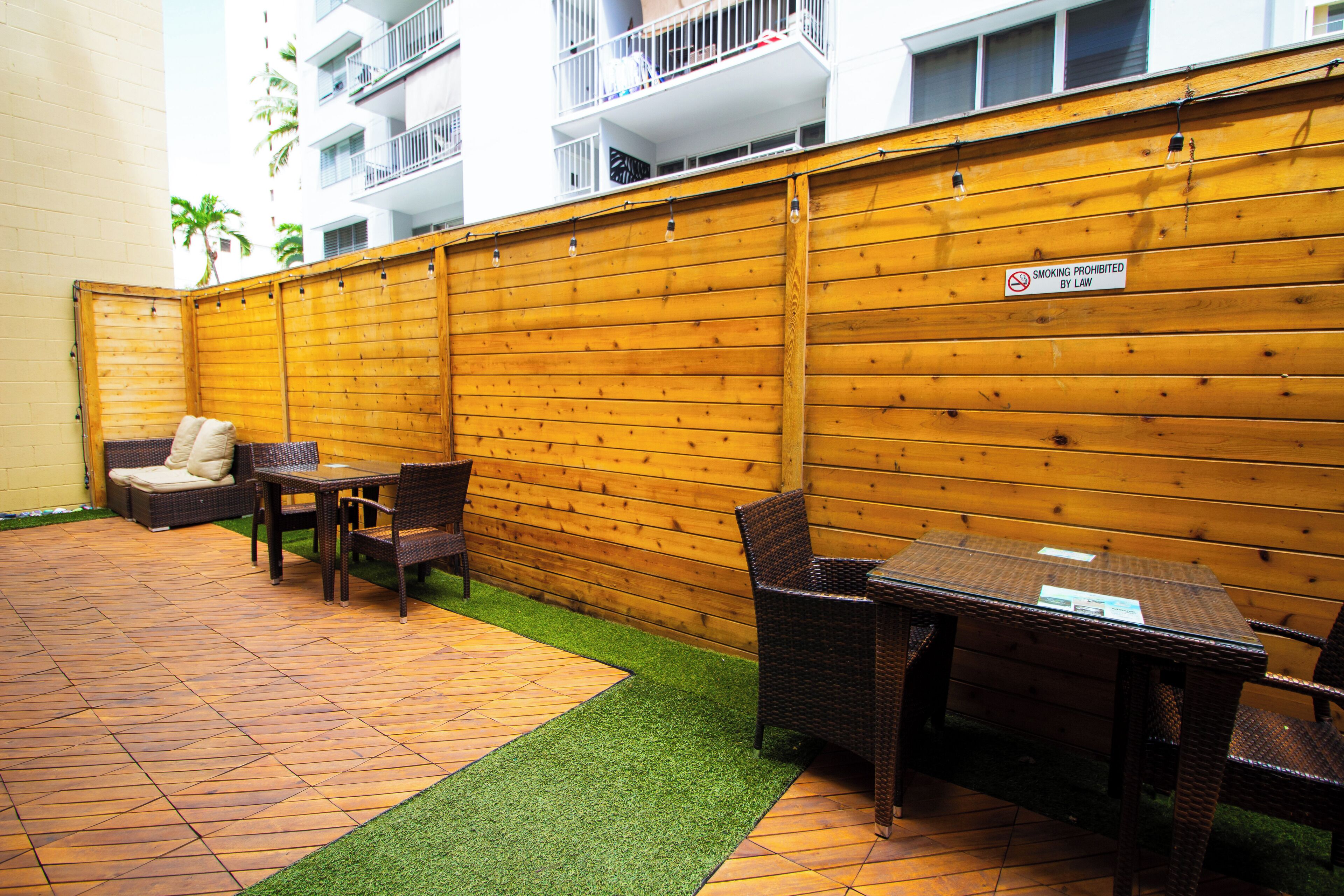An outdoor patio with a wooden fence, wicker furniture, and a sign prohibiting smoking.